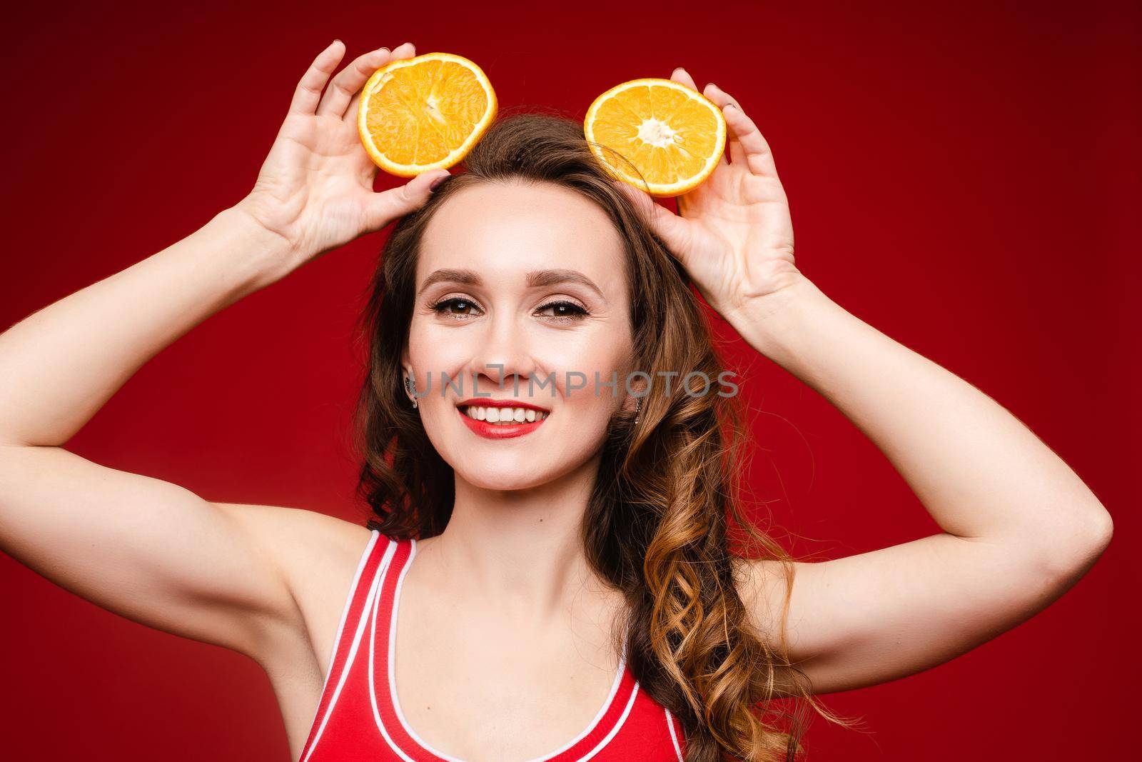 Beautiful woman in a red swimsuit with bright makeup and red lips with orange slices, summer, brightness, joy by StudioLucky