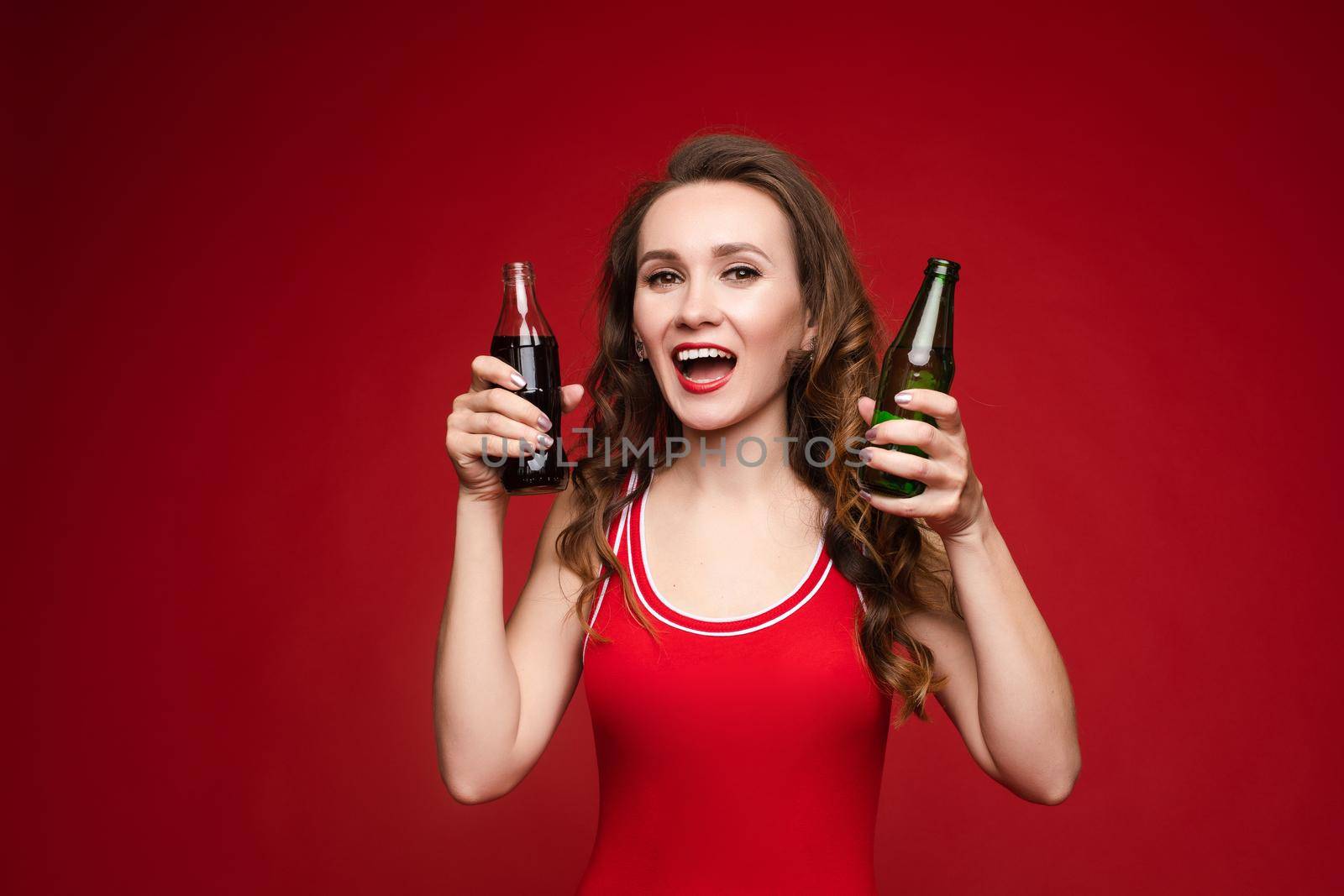 Beautiful woman in a red swimsuit with bright makeup and red lips with a bottle of soda,