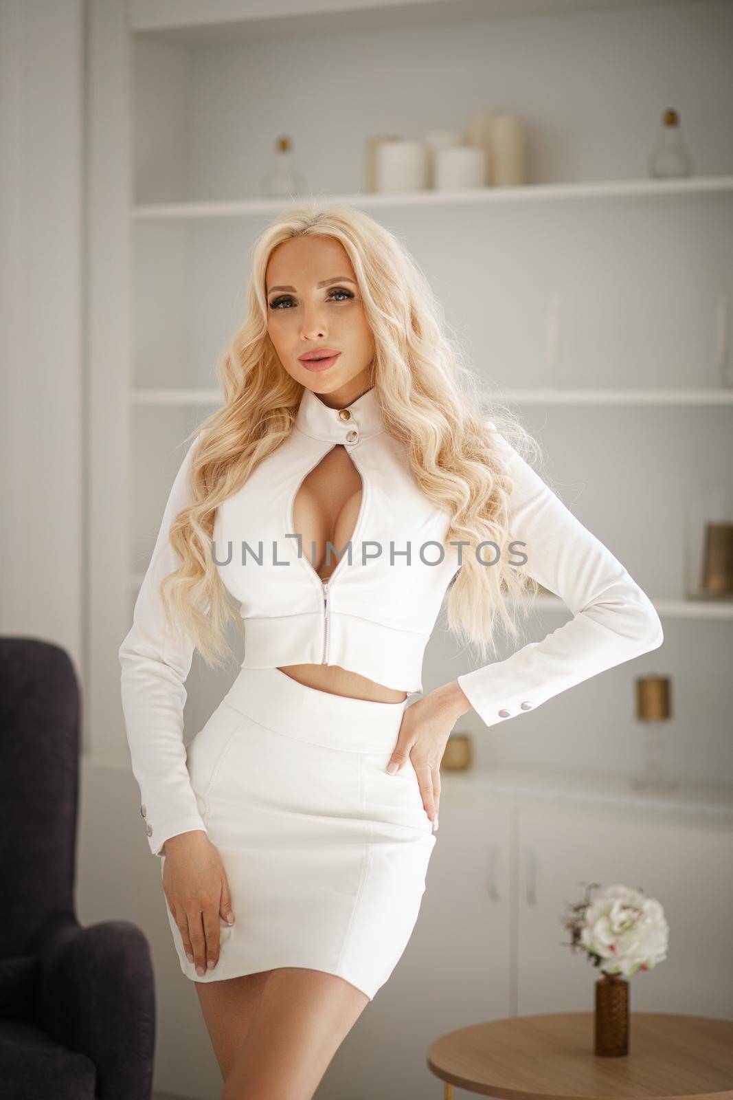 A very beautiful blonde woman in a white fashionable stylish suit in the studio. A charming woman looks and poses for the camera