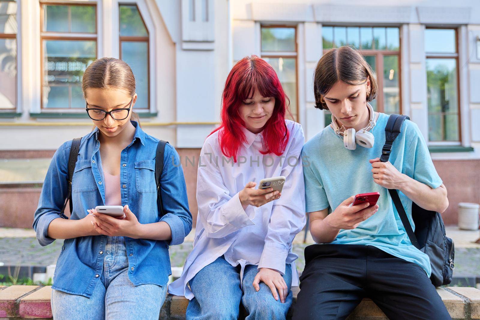 Teenage friends together outdoor having fun using smartphones on city street. Technology mobile apps, lifestyle, vacation leisure, urban style, youth concept