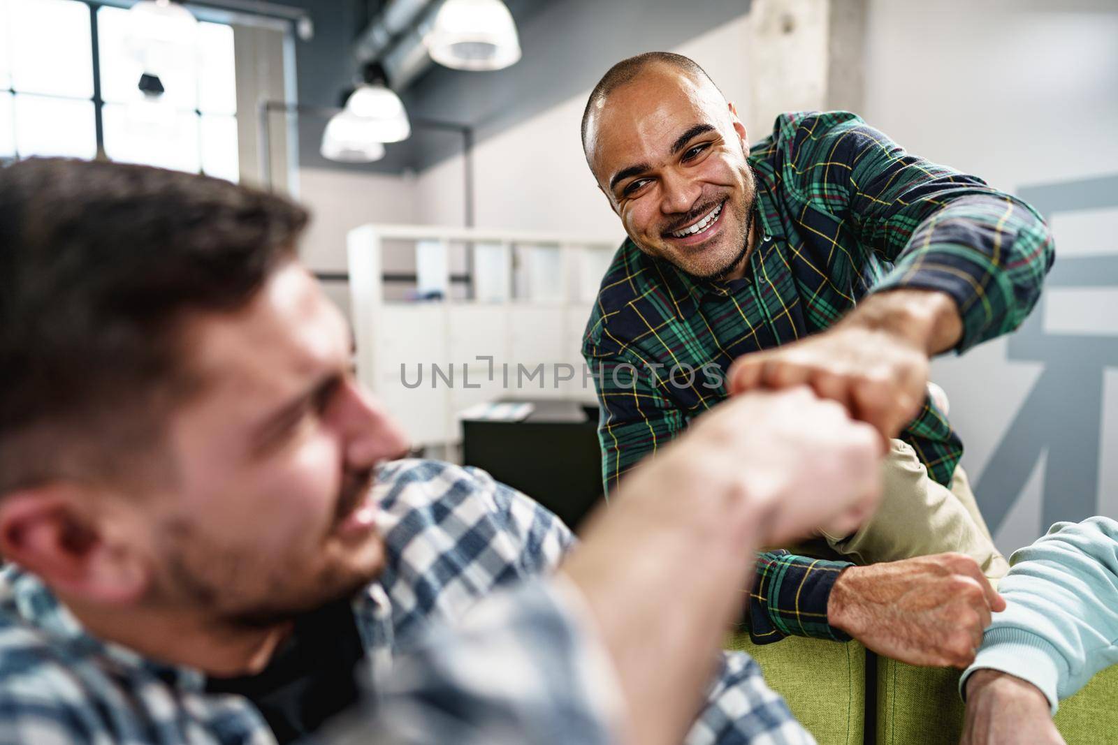Two handsome men sitting together in the office and giving each other a fist bump by Fabrikasimf