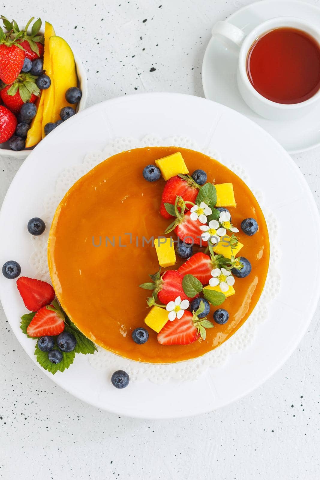 Mango cheesecake decorated with berries, mango slices and flowers on a stand. Vertical photo