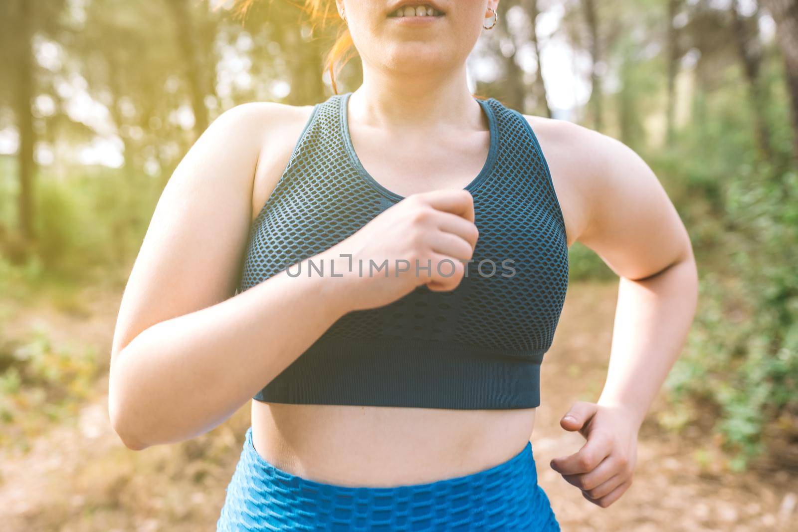 cropped shot young woman running through a forest on a summer day. female athlete doing sport outdoors. wellness and healthy living concept. outdoors, natural sunlight.