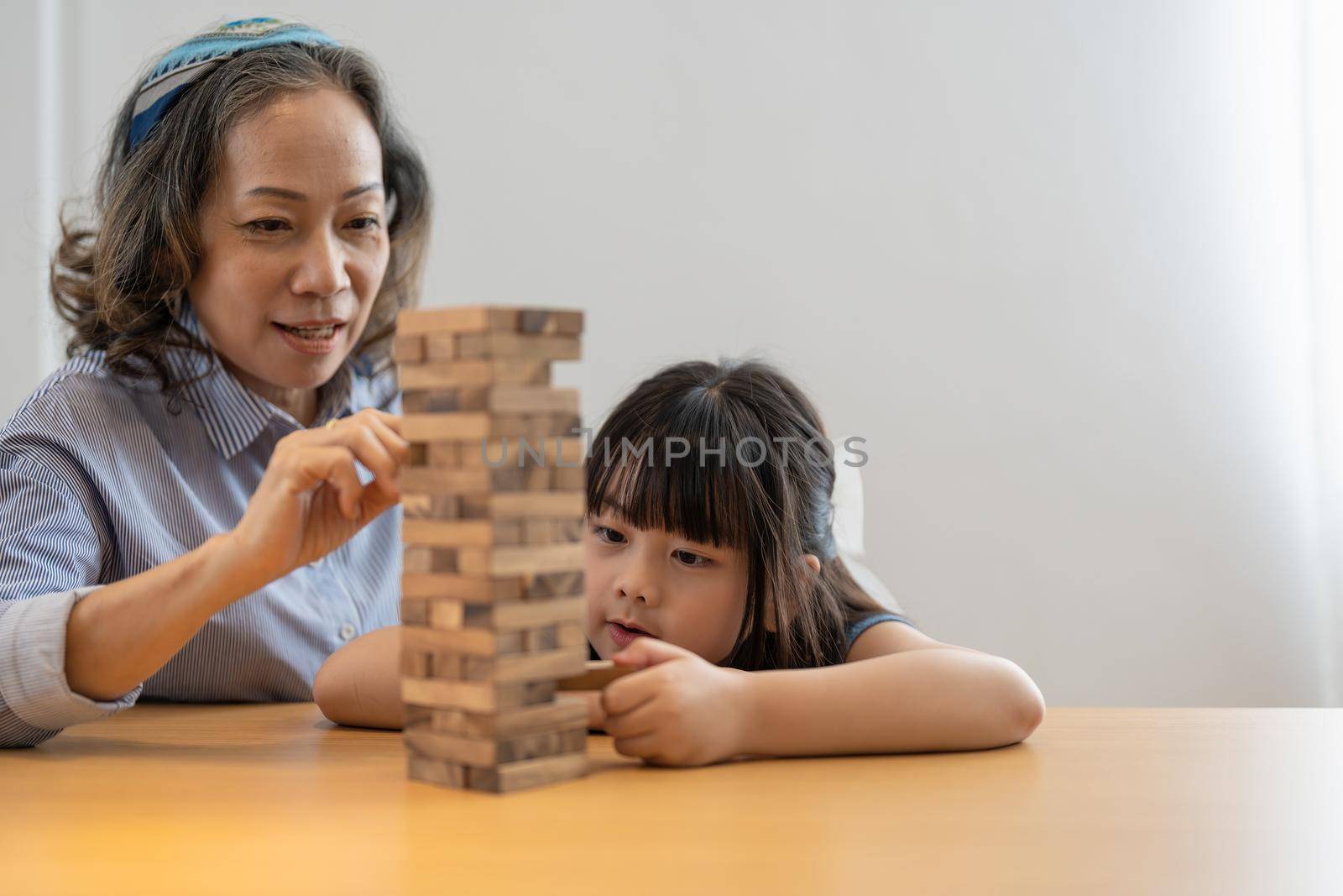 Happy moments of Asian grandmother with her granddaughter playing jenga constructor. Leisure activities for children at home. by nateemee