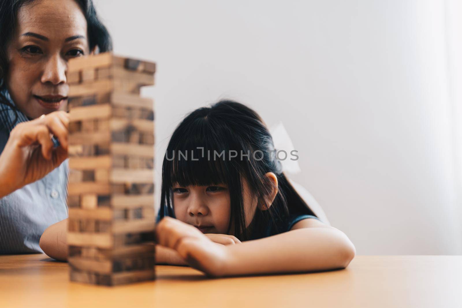 Happy moments of Asian grandmother with her granddaughter playing jenga constructor. Leisure activities for children at home. by nateemee
