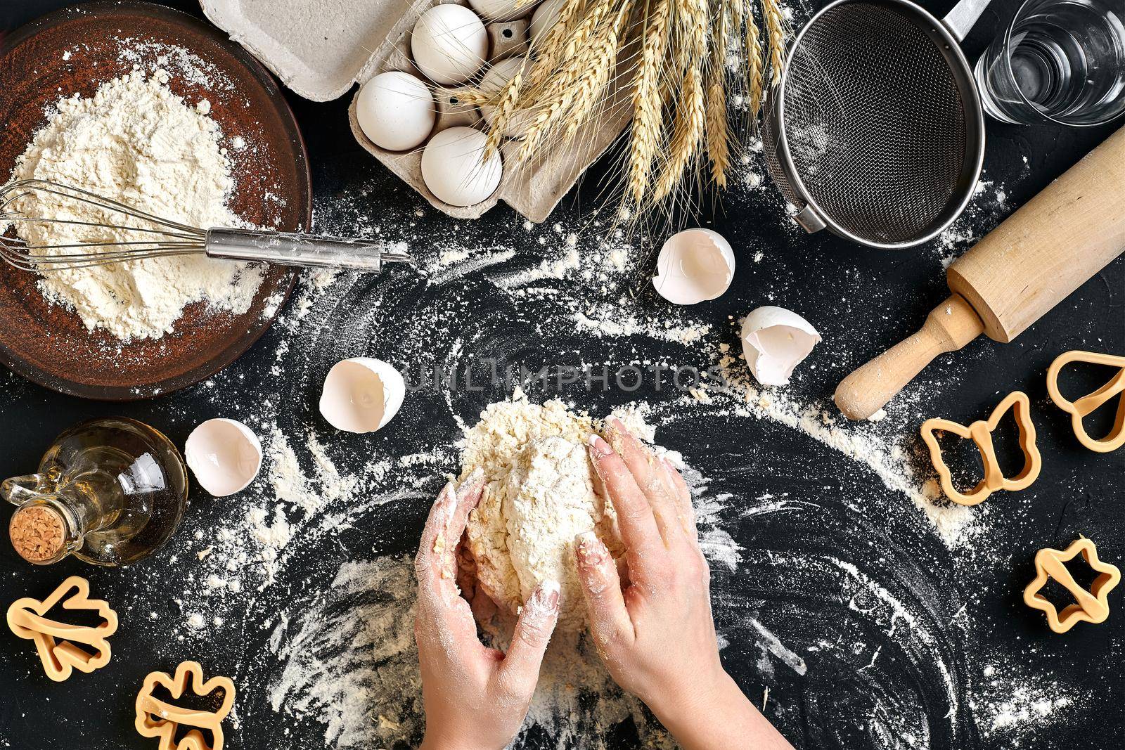 Woman's hands knead dough on table with flour, eggs and ingredients on black table. Top view. Still life. Flat lay