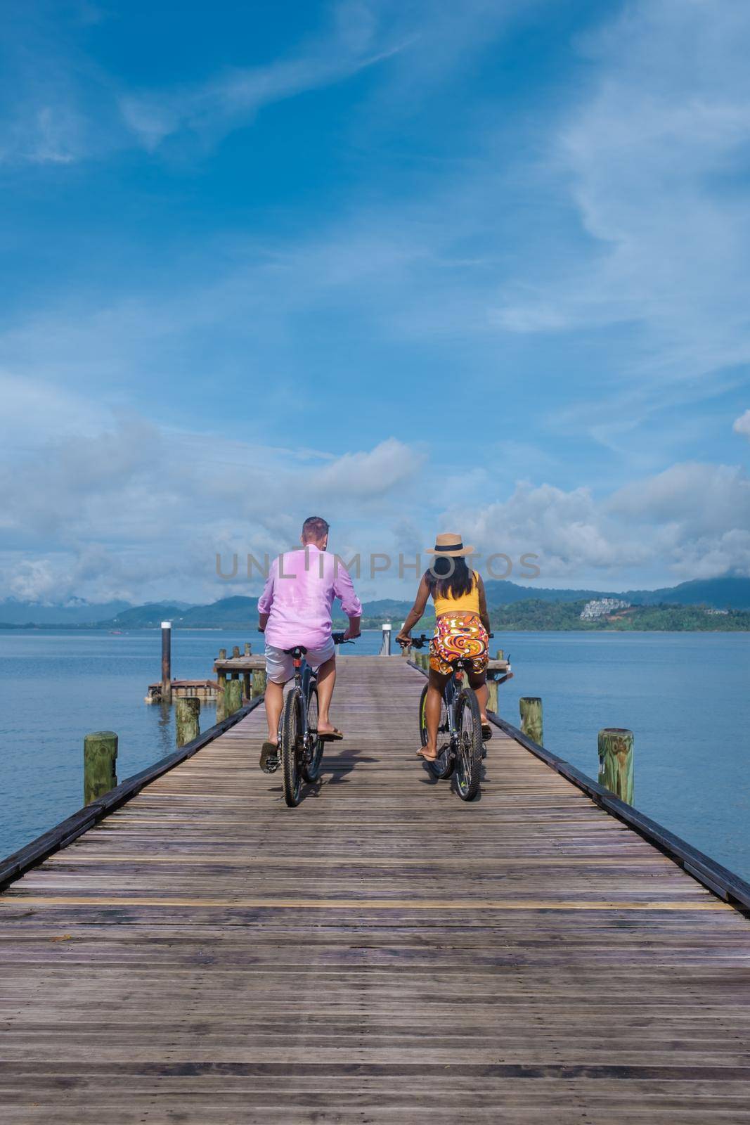 men and woman on a bicycle, a couple of men and woman on a tropical island with a wooden pier jetty in Thailand Phuket Naka Island.