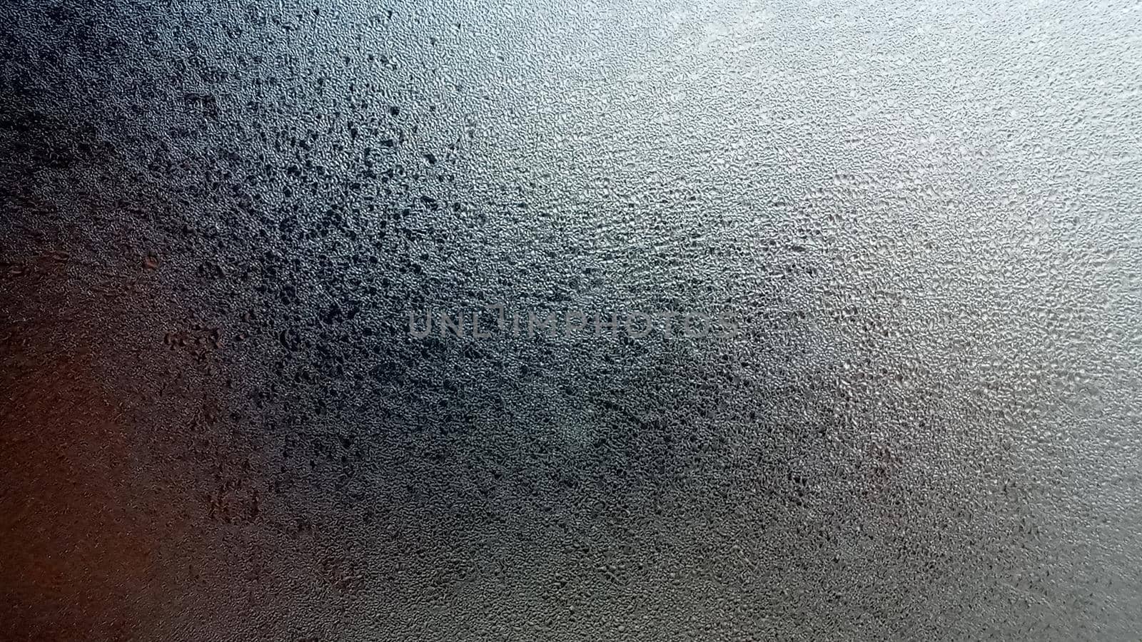 Abstract frosty pattern on glass, background texture. Frozen windshield. Granular structure of transparent ice. The sky is shining through. Abstract ice background.