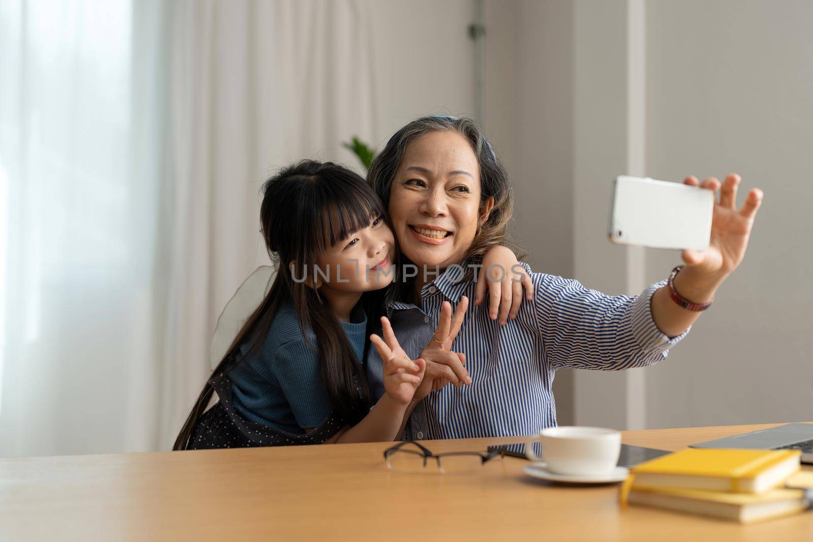 Happy asian smiling older grandma and child girl having fun taking selfie on phone, cheerful granny with little kid play making photo on mobile.