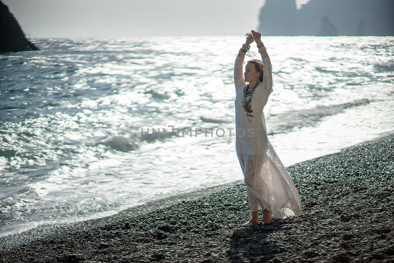 Middle aged woman looks good with blond hair, boho style in white long dress on the beach decorations on her neck and arms