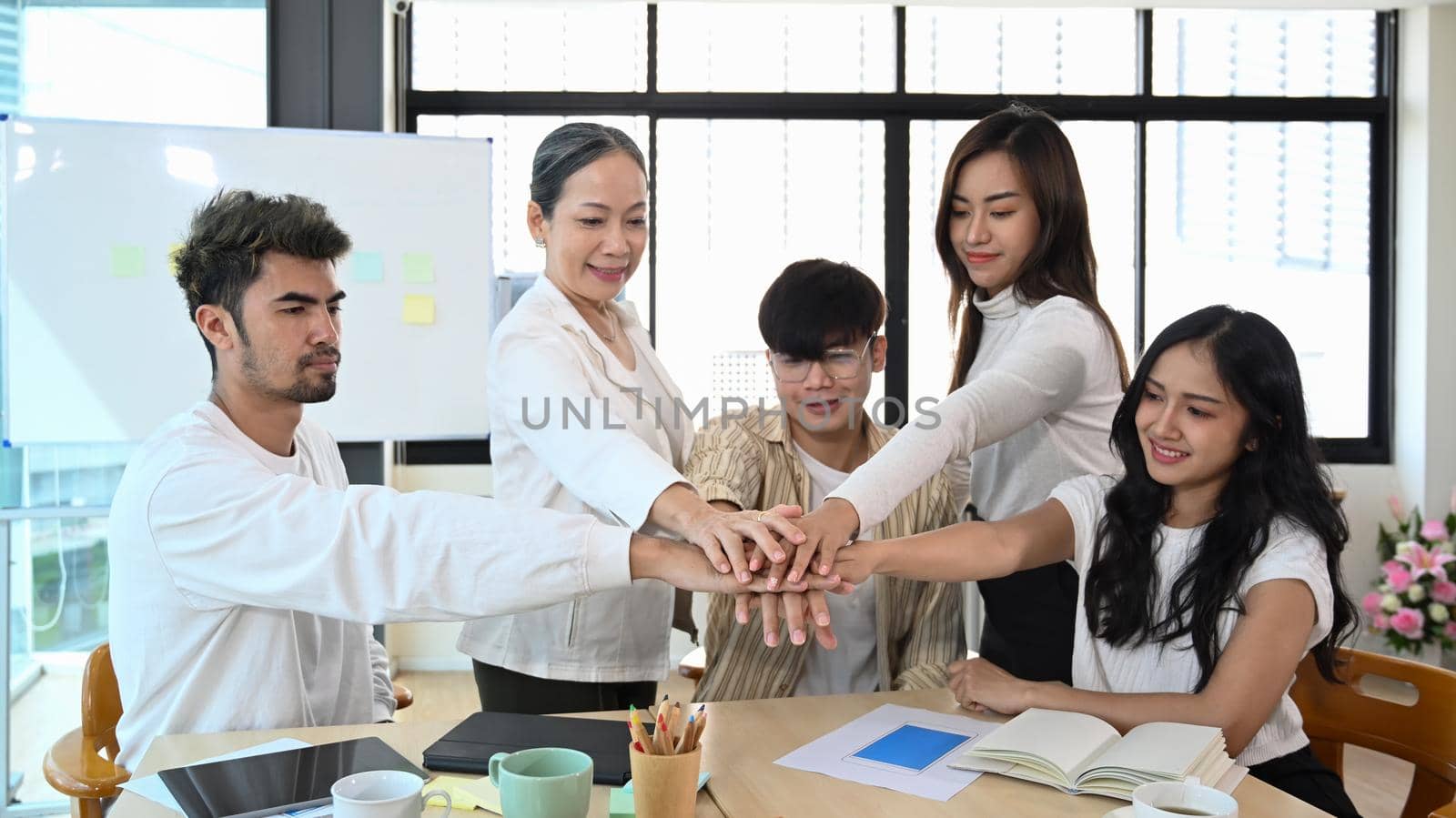 Happy motivated business people stacking hands together, showing support and team spirit together, celebrating corporate achievement at meeting.