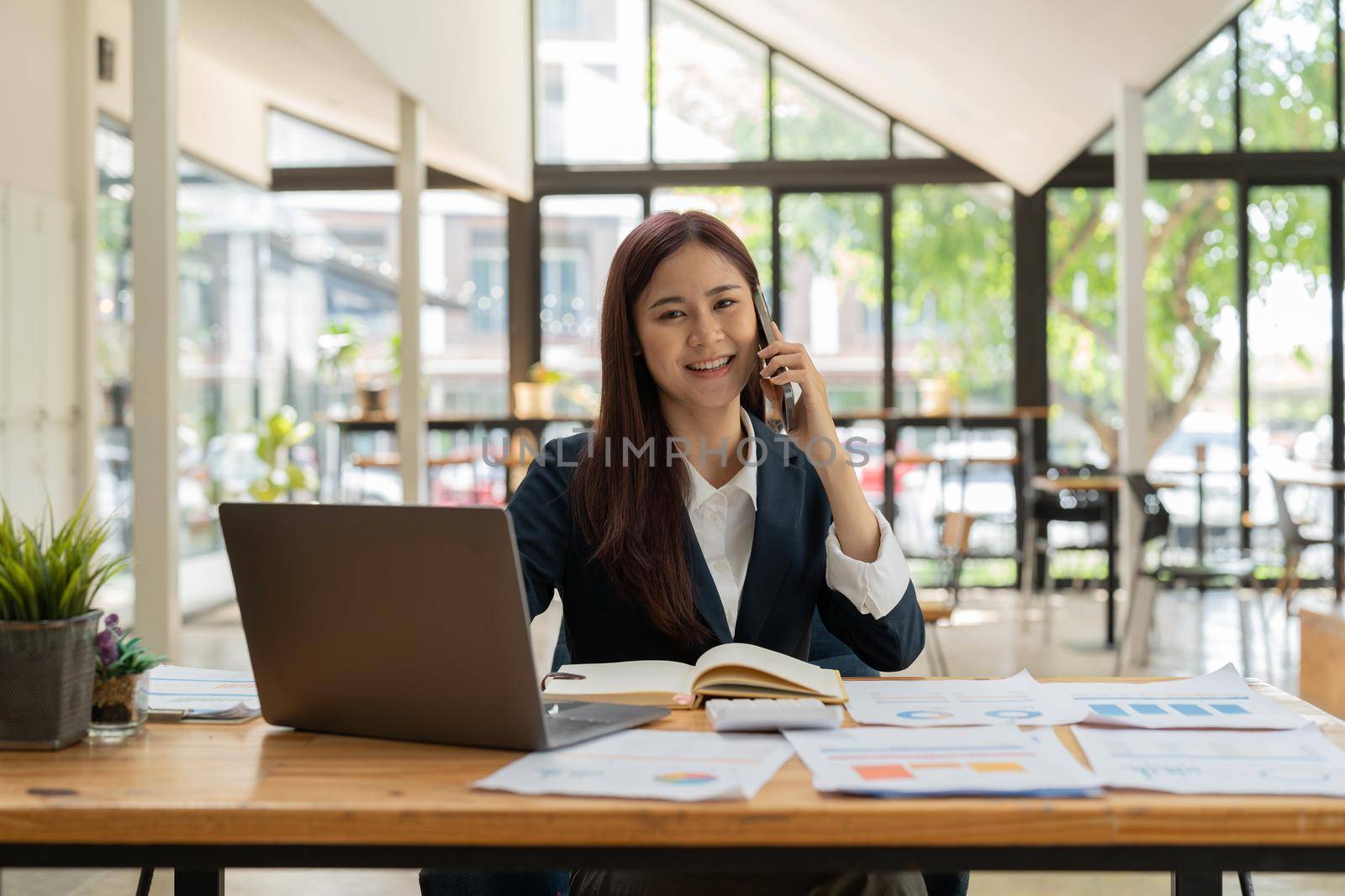 Smiling business asian woman in black suit talking on phone.