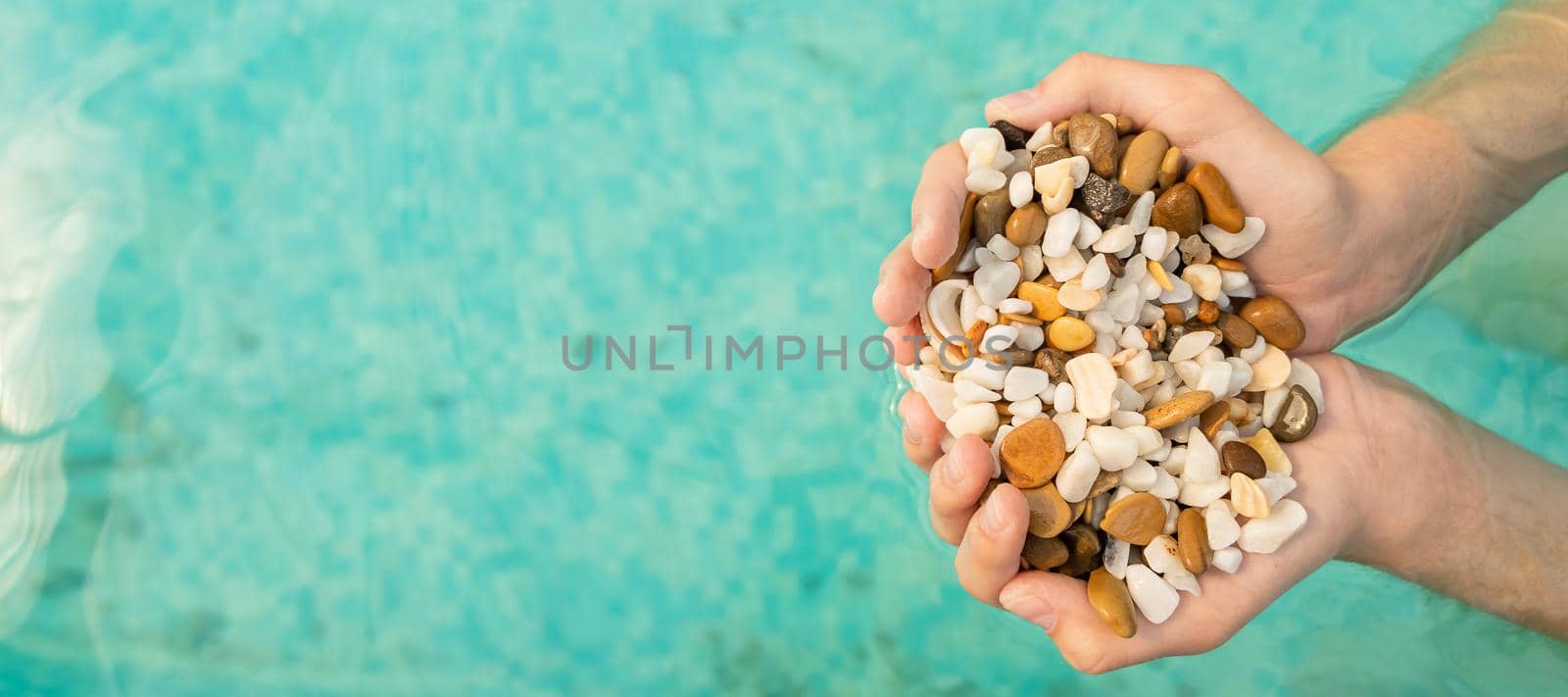 banner with children's hands holding a full handful of sea pebbles on a background of blue water. concept of summer and vacation at sea. flat lay