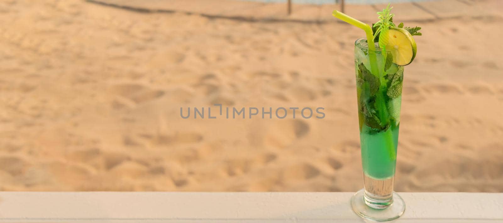 banner with tropical green cocktail with straw, mint and lime on background of golden sand. the concept of relaxing and eating by the sea on a bright, hot and sunny day on the beach. copy space