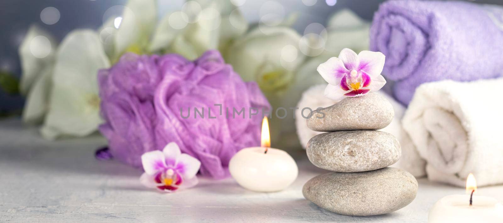 banner with massage stones, burning candles, rolled towels, flowers, abstract lights. Spa resort therapy composition in lilac colors Soft focus