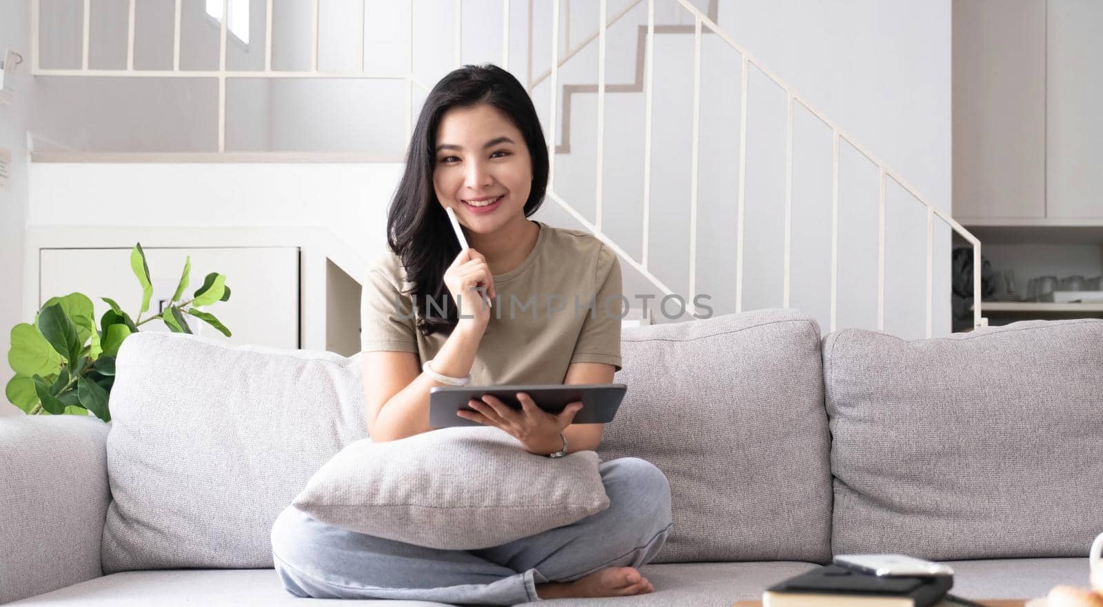 Beautiful smiling Asian woman looking at camera relaxing on leather sofa at home. work on a laptop computer.