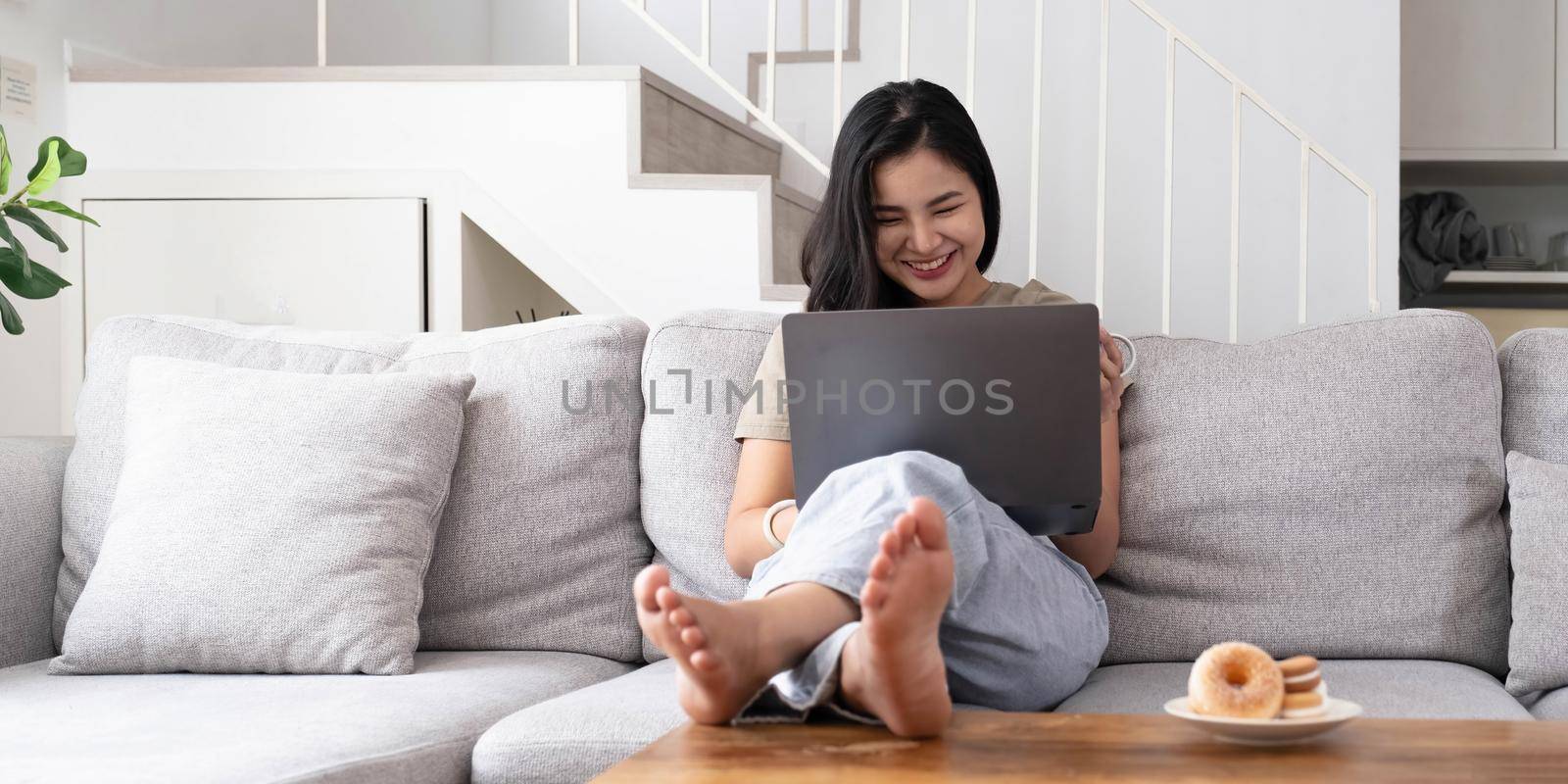 asian young woman looking laptop laughing with good news or discount voucher for shopping online at home.Happy and cheerful woman looking on laptop read message feel excited by wichayada