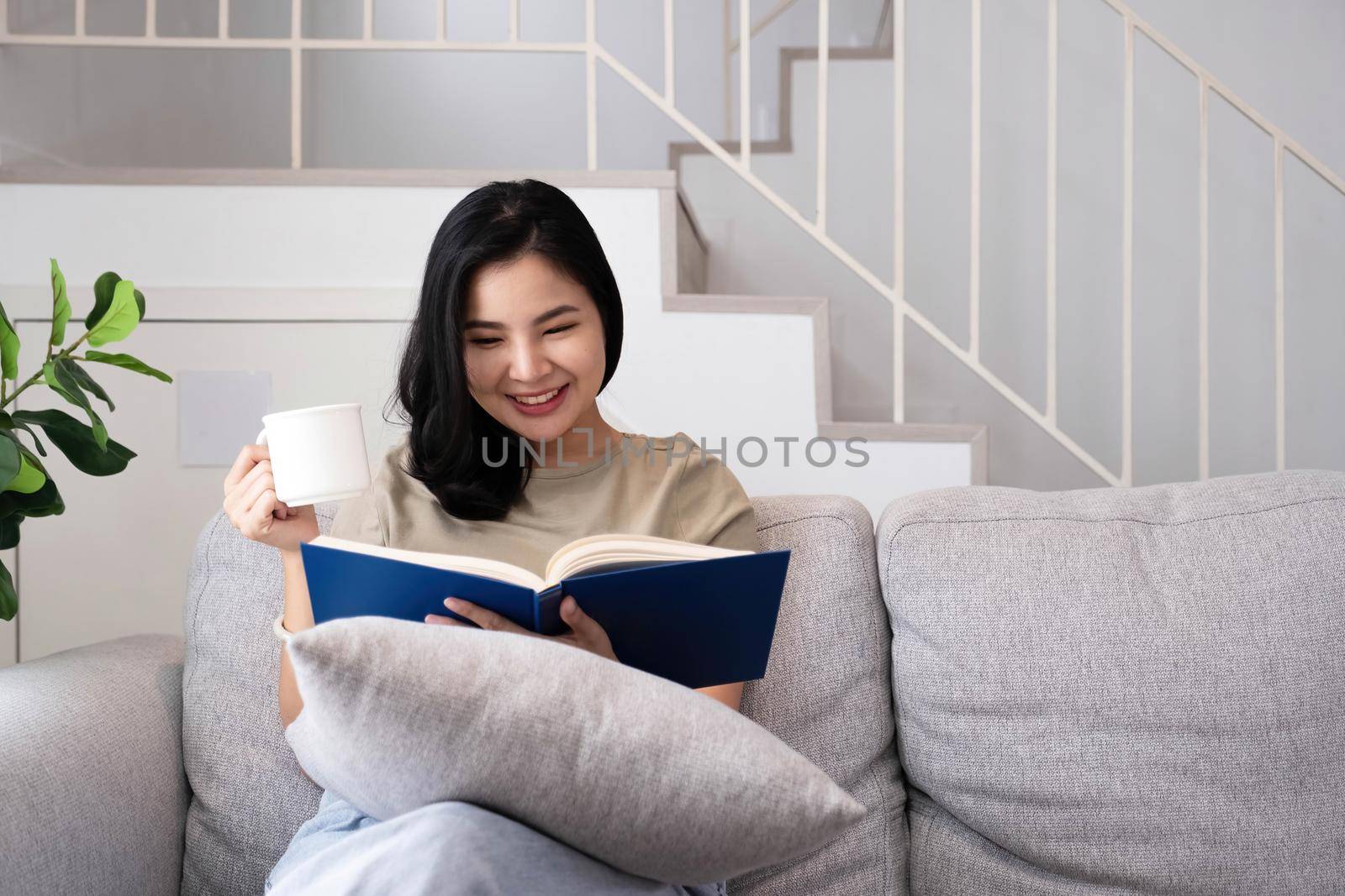 young woman relaxing and drinking hot coffee or tea reading a book happily by wichayada