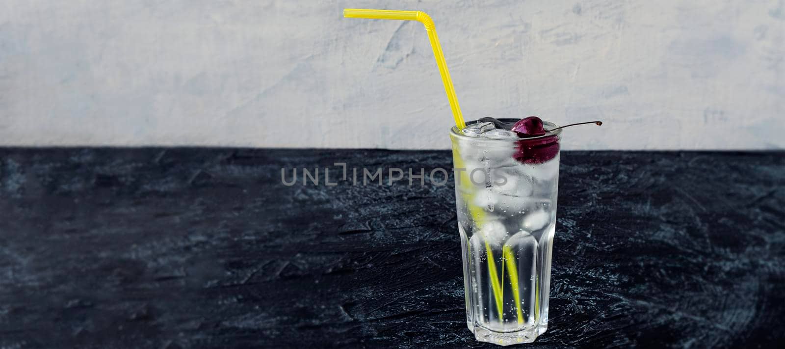 banner with Clear glass with cherry, ice and yellow cocktail straw on black and white background. Summer cold drink and cocktail. copy space