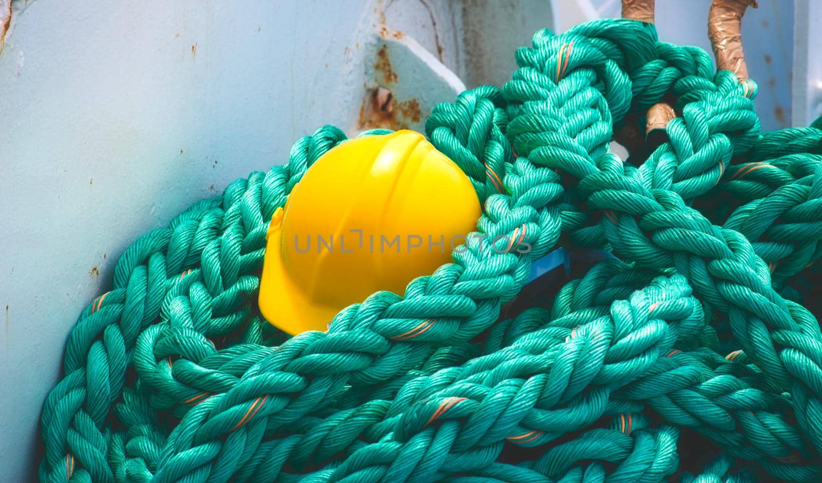 Yellow hard hat lying on curled heavy duty rope on board a sea vessel