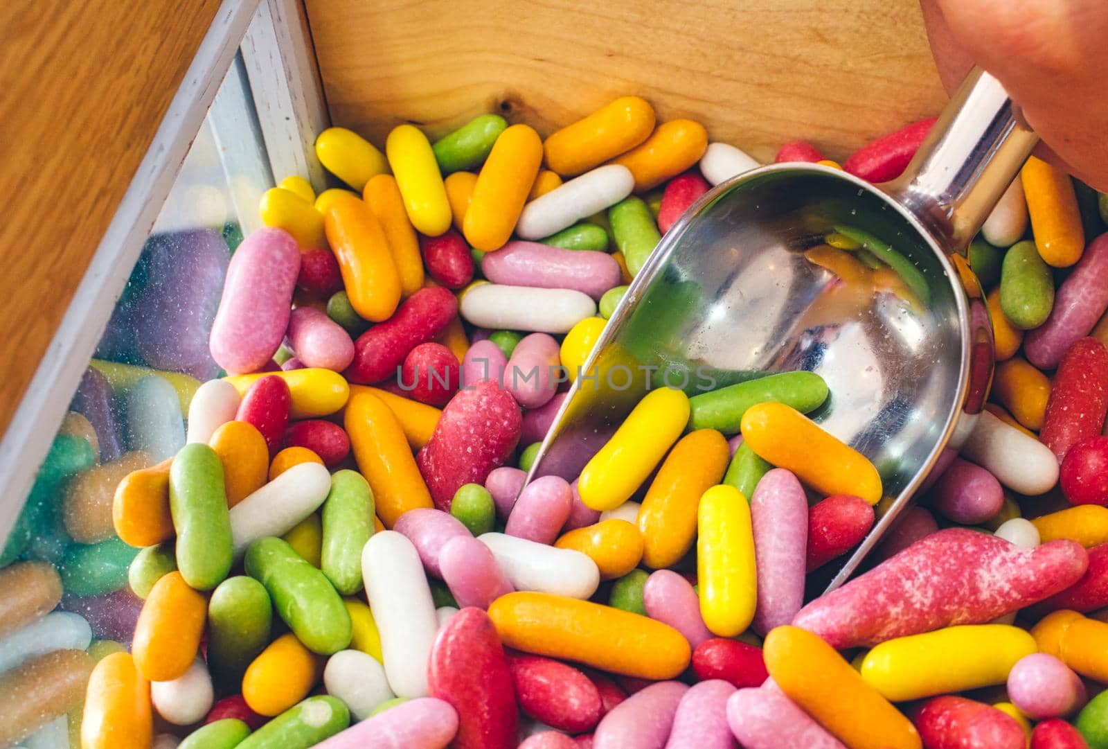 Close-up of multi-colored candy sticks / sweets with a hand filling a scoop from a wooden box
