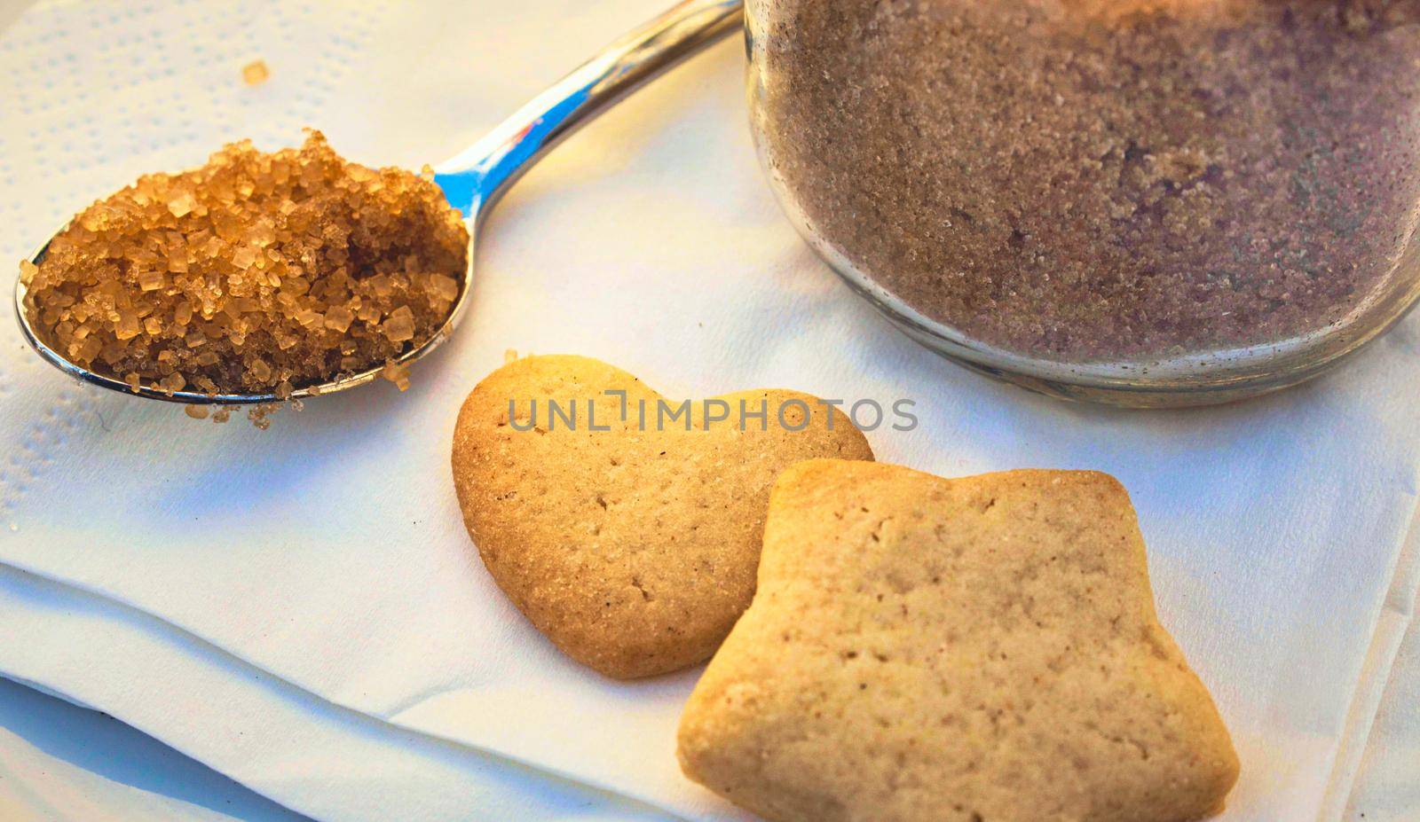 Brown sugar in a teaspoon for tea or coffee with heart and star shaped biscuits on a table in a cafe