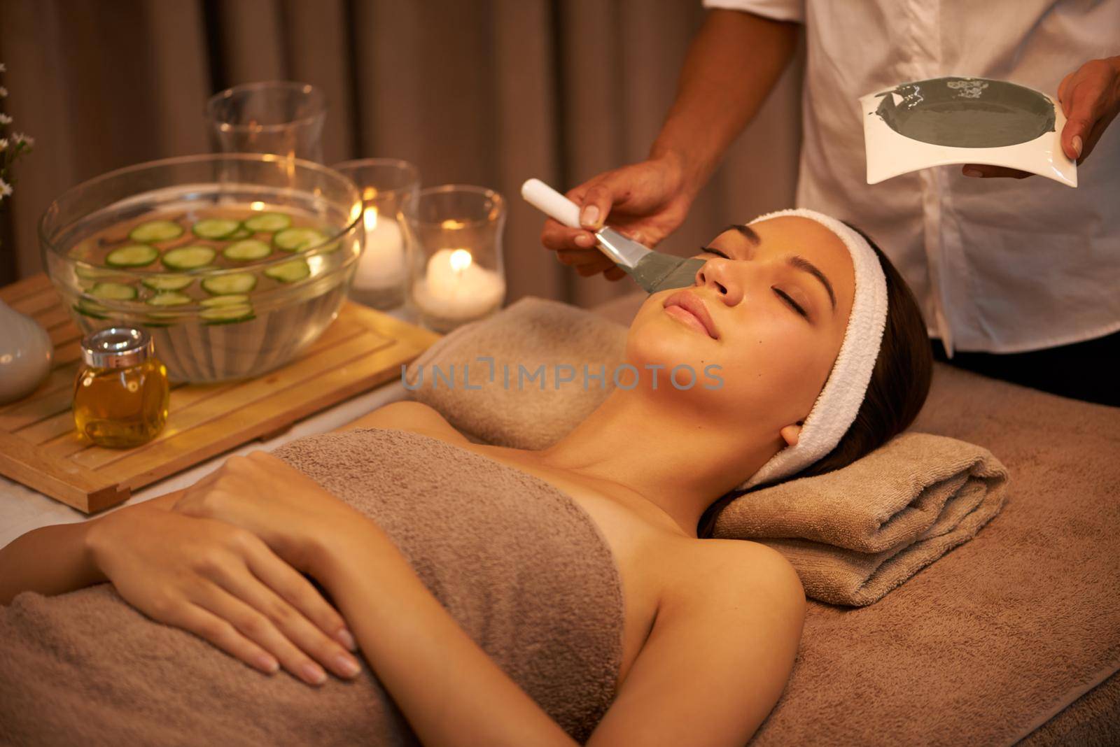 A young woman lying in a day spa with a face mask being applied.