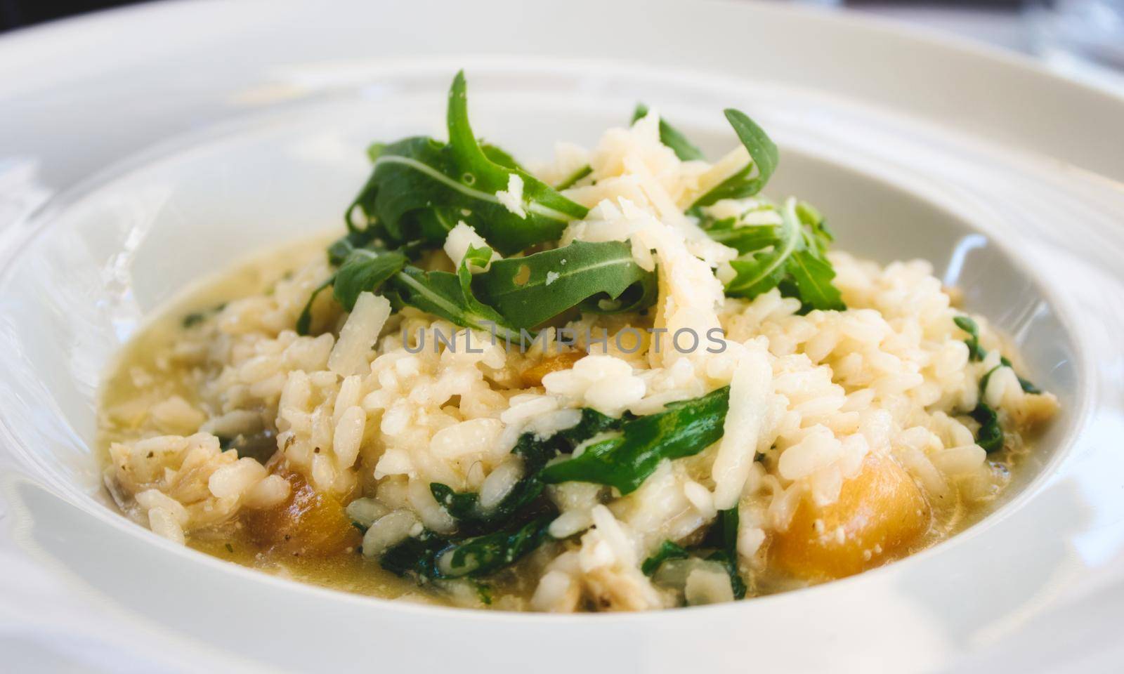 Pumpkin risotto with rocket leaves and parmesan cheese shavings in a white dish