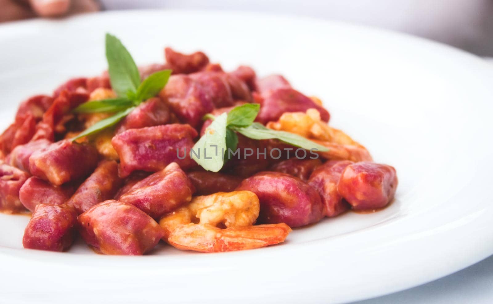 Beetroot gnocchi and prawns garnished with mint on a white plate