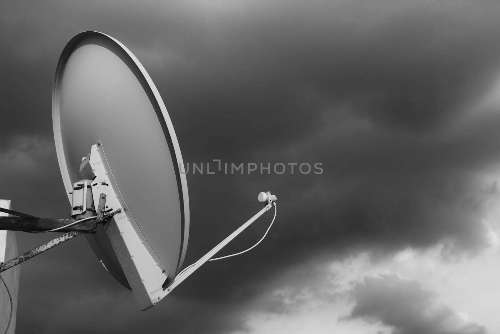 Black and white satellite dish on a rooftop against a cloudy moody sky background