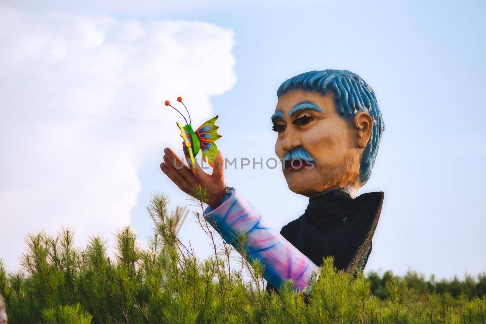 Giant fibre glass statue of a man holding a colorful butterfly outdoors in a field