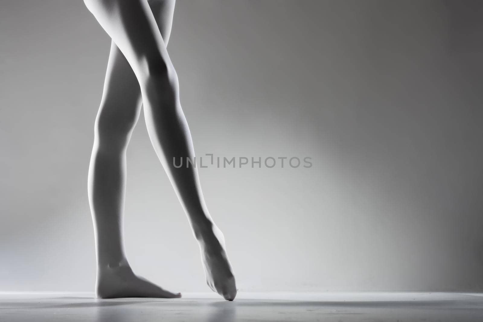Sexy female legs with white leggings standing ballerina pose on gray background.