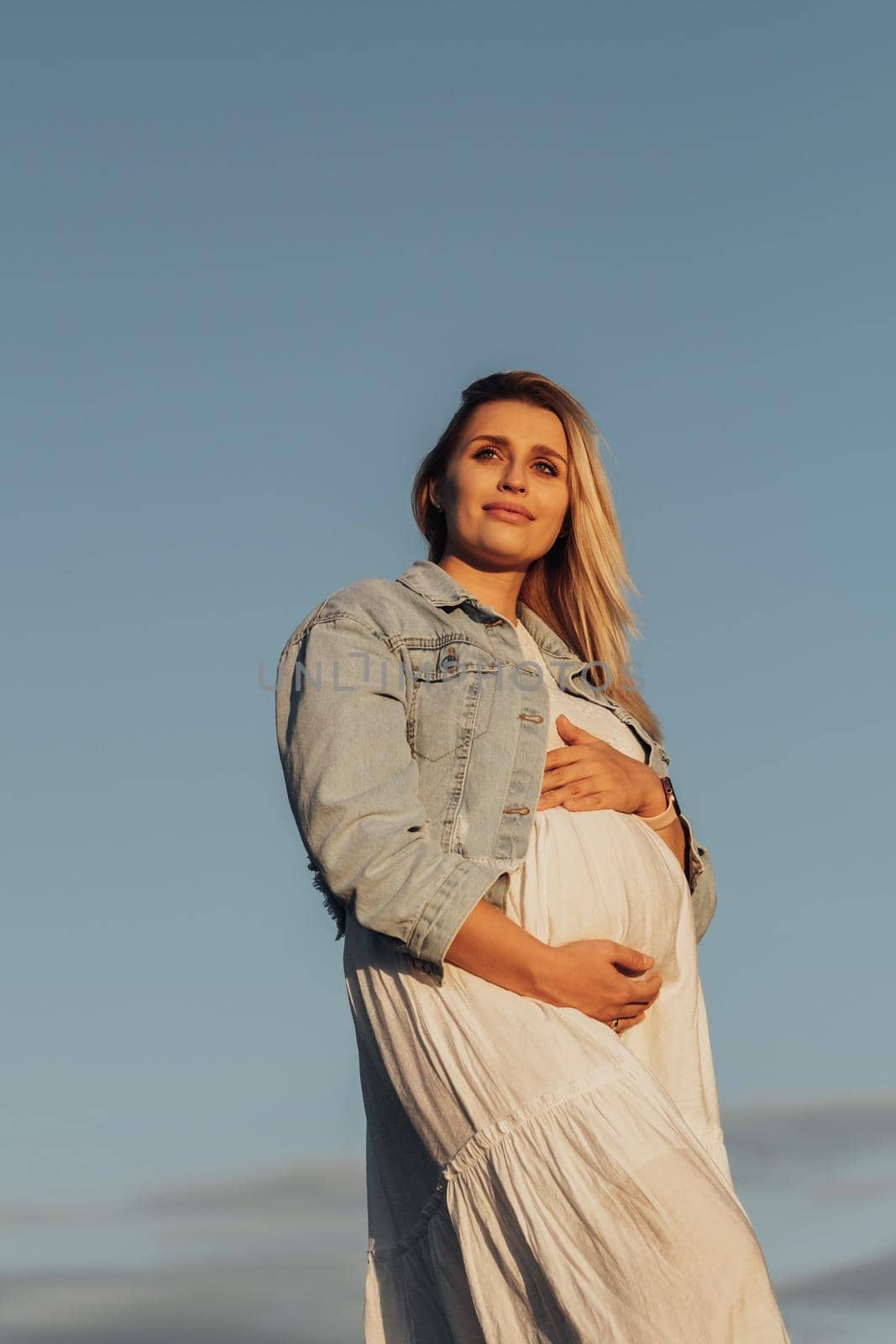 Portrait of Pregnant Young Caucasian Woman Holding Her Belly on Background of Blue Sky
