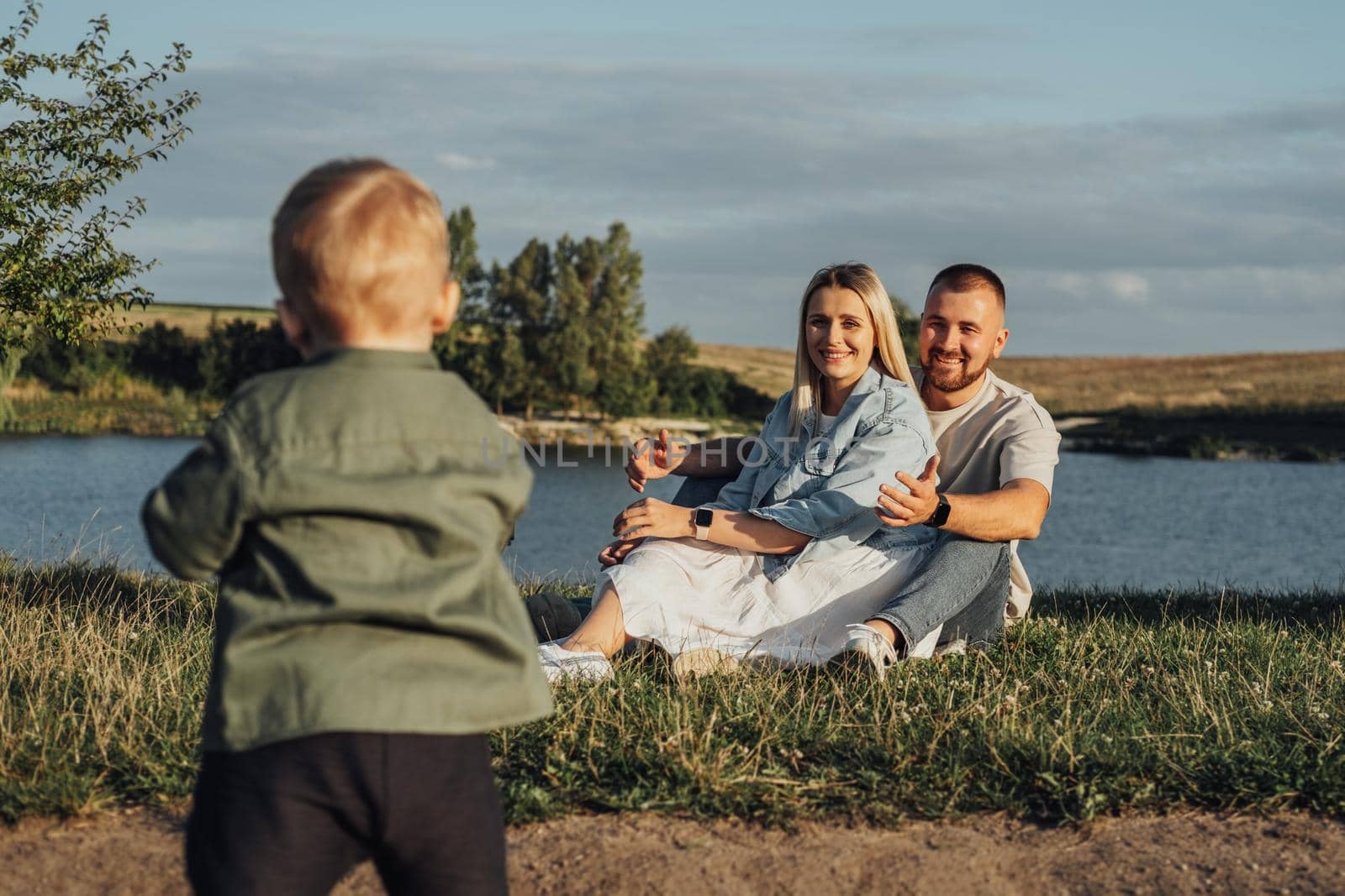 Happy Young Family, Mother and Father with Their Toddler Son Enjoying Weekend Outdoors Near Lake