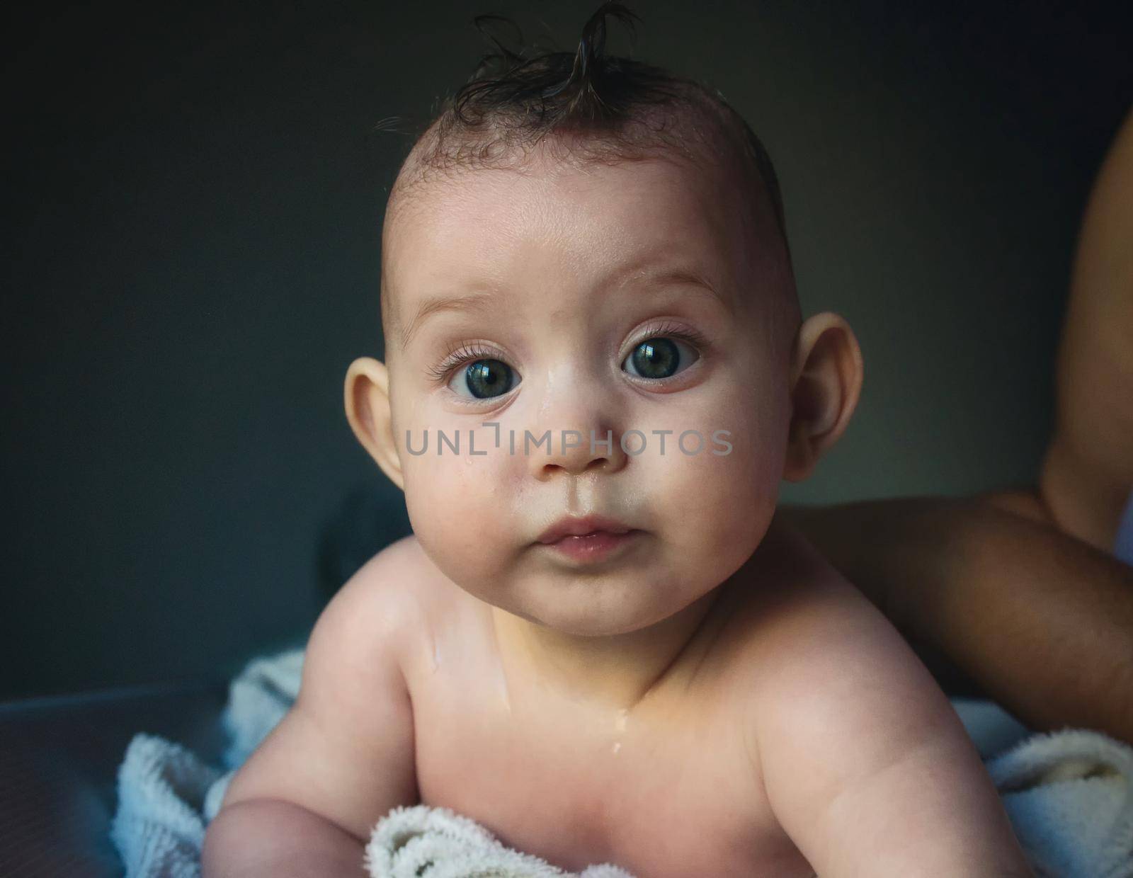 Cute newborn baby just out of the bath with wet hair and face looking at the camera