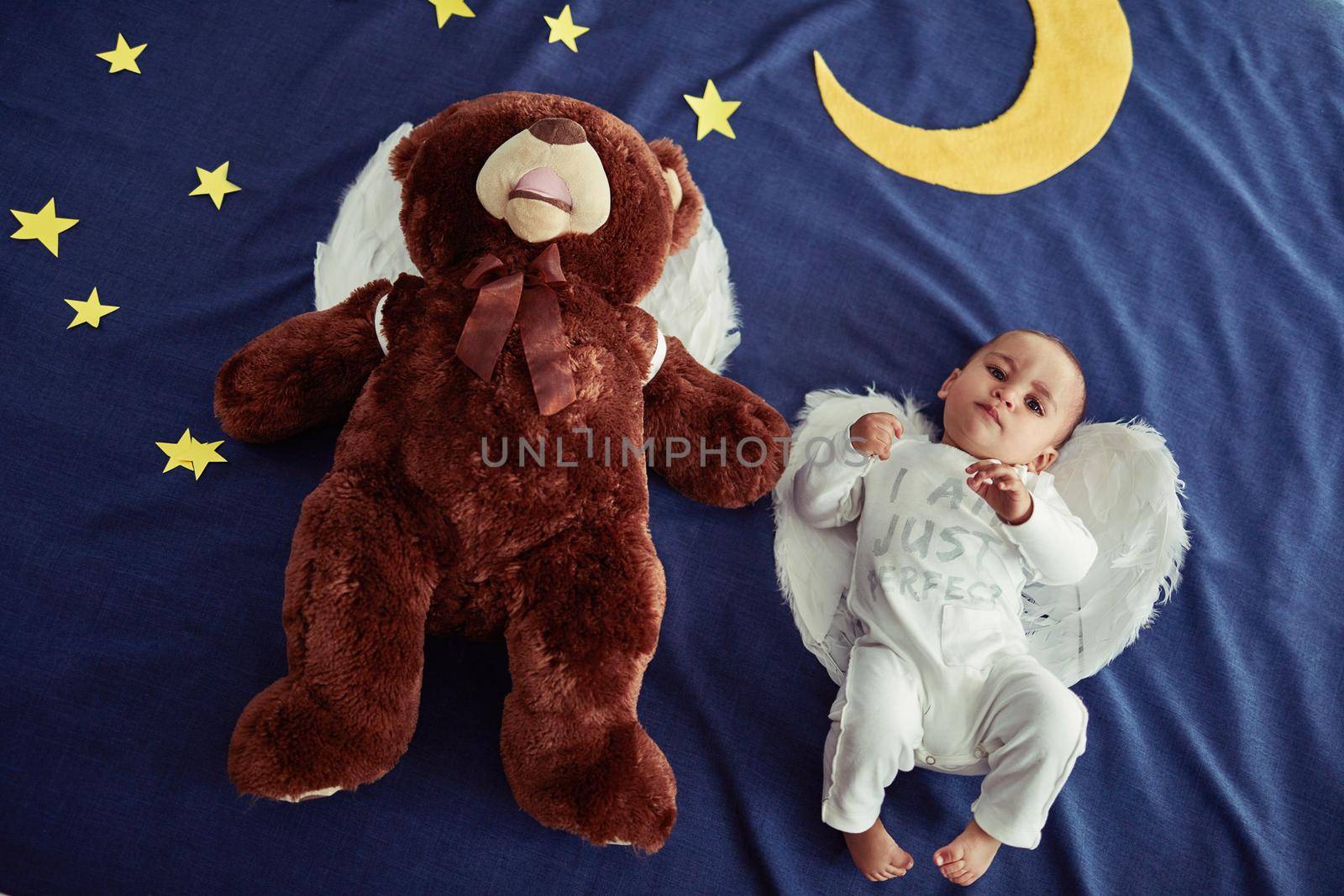 Babies are angels sent from heaven. Concept shot of an adorable baby boy and a teddy bear wearing angel wings against an imaginary night time background. by YuriArcurs