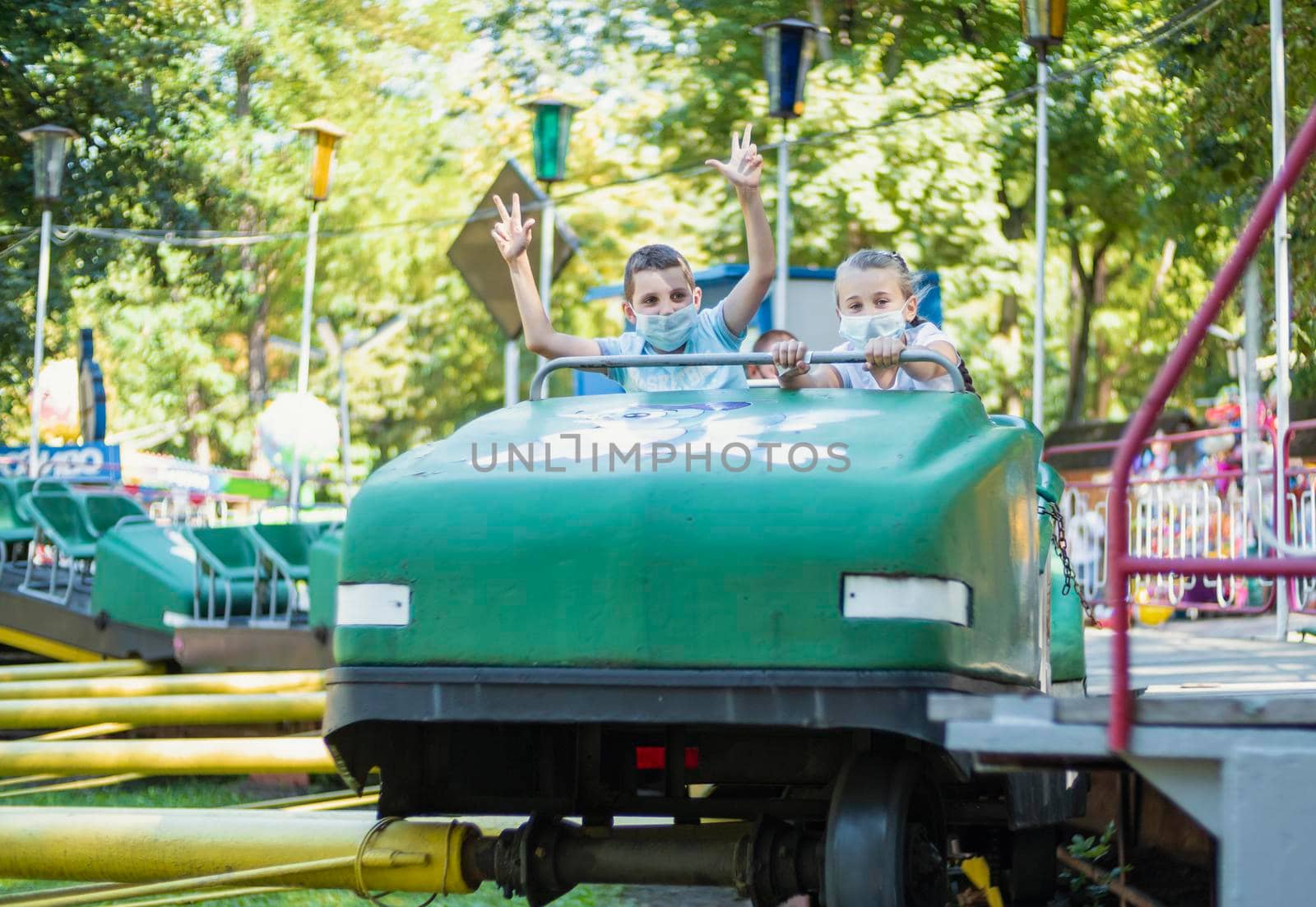 children in medical masks ride an attraction train