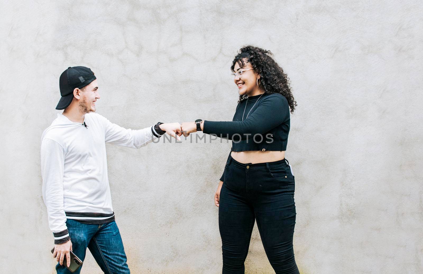 Two teenage friends bumping their fists. A guy and teenage girl shaking fists at each other, close up of two funny friends bumping fists in a friendly way by isaiphoto