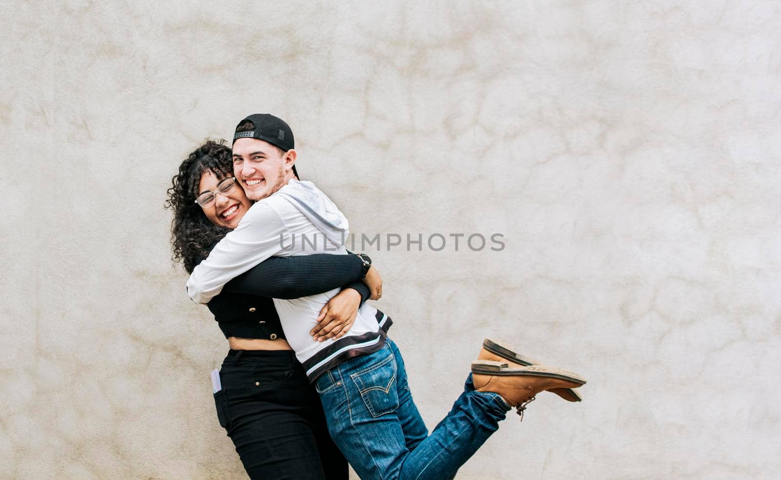 Two teenage friends embracing fraternally, Young happy couple embracing looking at camera outdoors, Teenage couple embracing happily looking at camera by isaiphoto