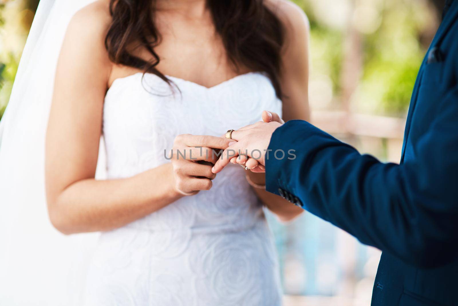 With this thing I vow to always love you. Cropped shot of an unrecognizable bride slipping a ring on to her grooms finger while standing outdoors on their wedding day. by YuriArcurs