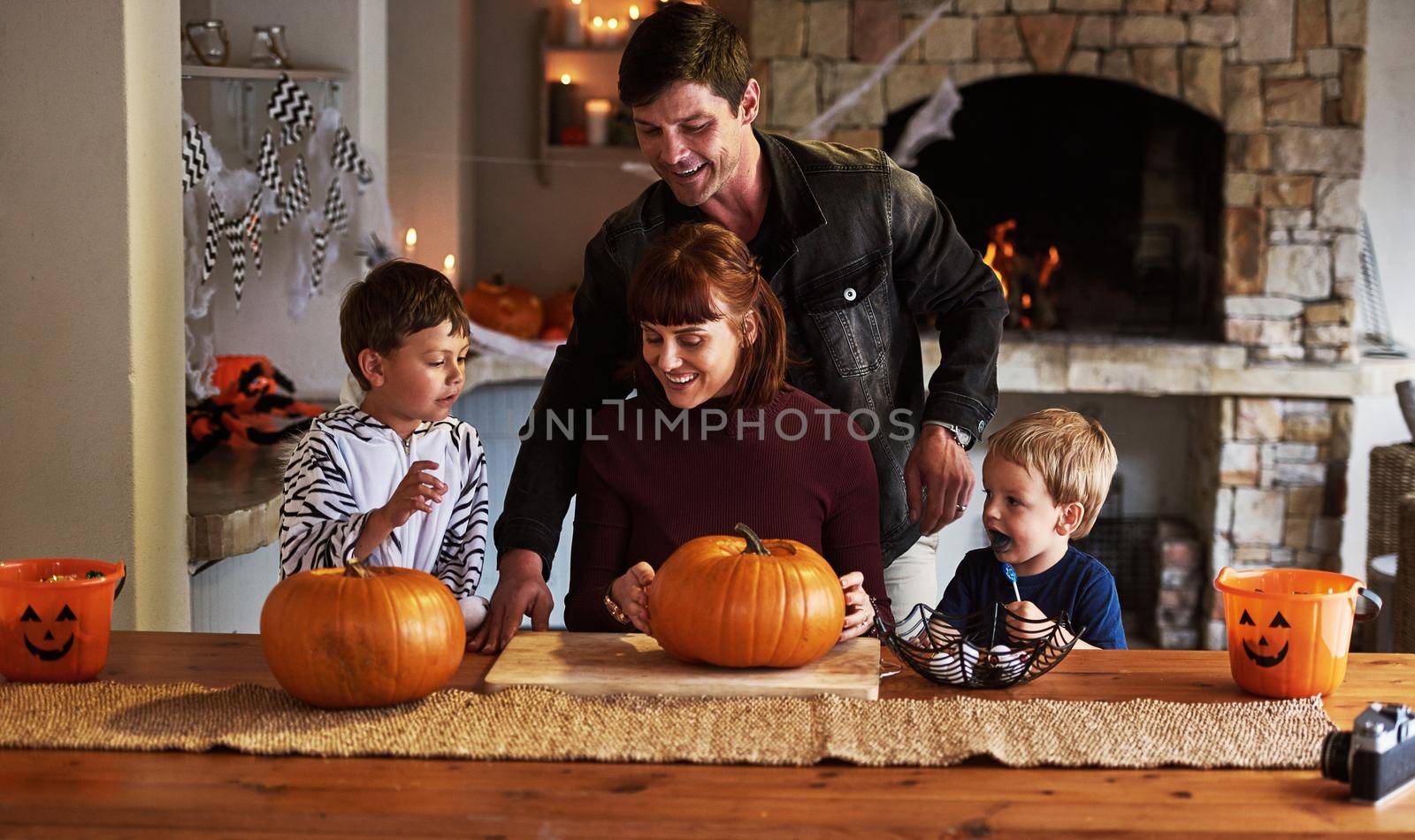 Time to carve out the good times. Shot of an adorable young family carving out pumpkins and celebrating halloween together at home. by YuriArcurs