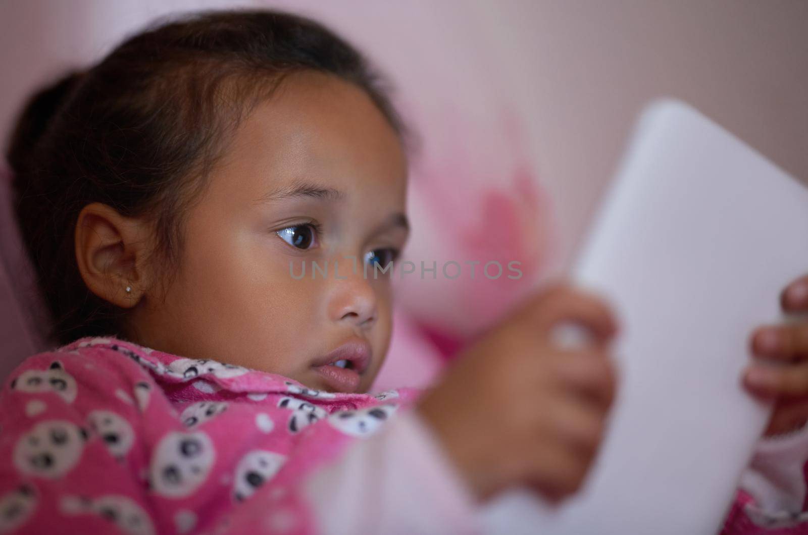 Shes a curious little one. Shot of a little girl lying in bed using a digital tablet. by YuriArcurs