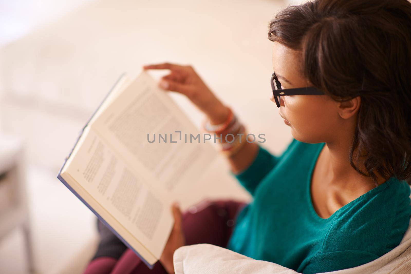 Shot of a young woman reading a book on the sofa at home.