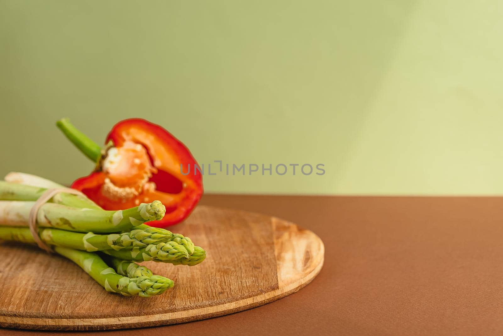 Vegetables lie on a wooden board: tomatoes, asparagus, cucumbers, red bell peppers. brown, light green background. place for text