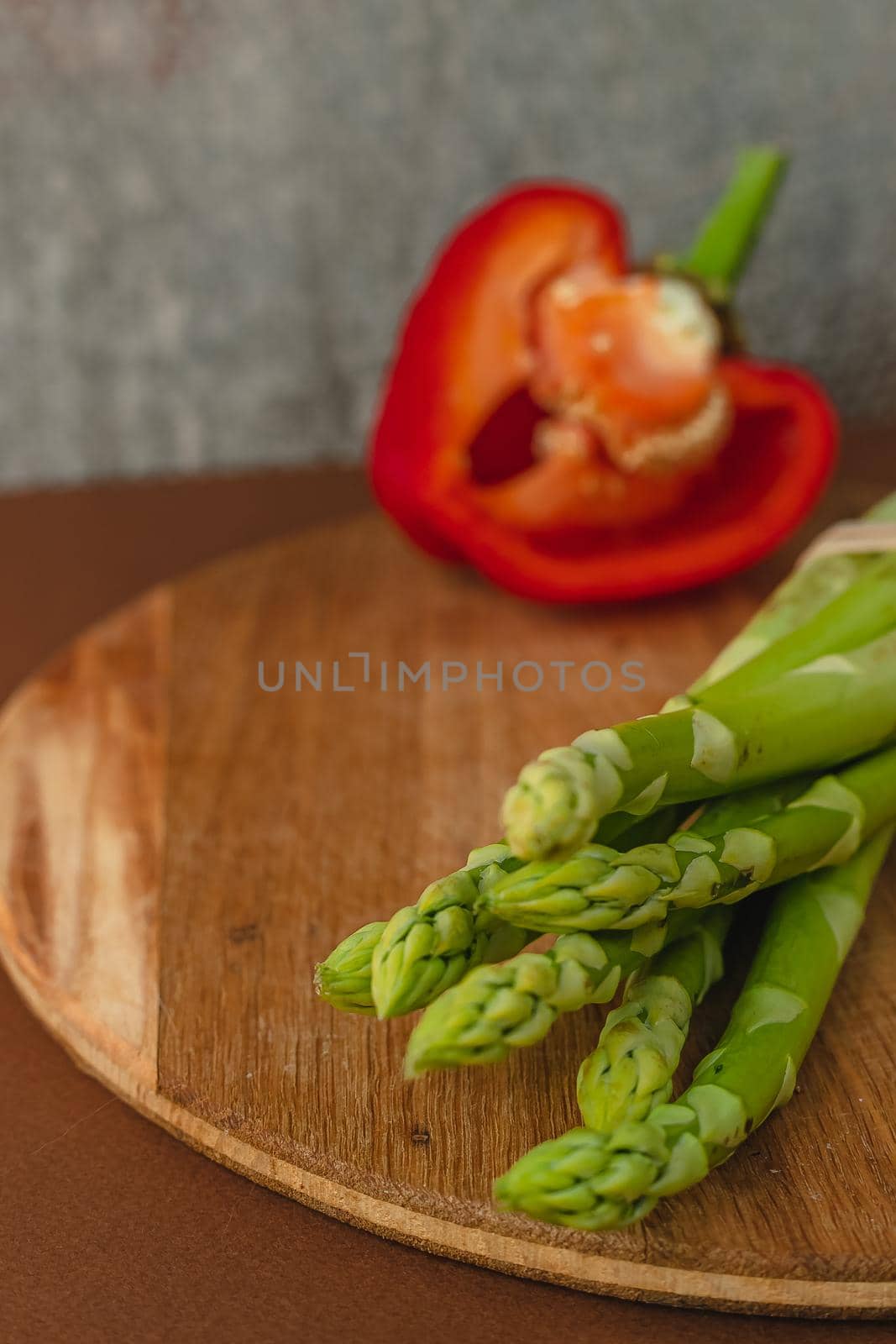 branches of fresh green asparagus on a wooden board, red big pepper on the background. brown background, top view. Basic trend concept with copy space