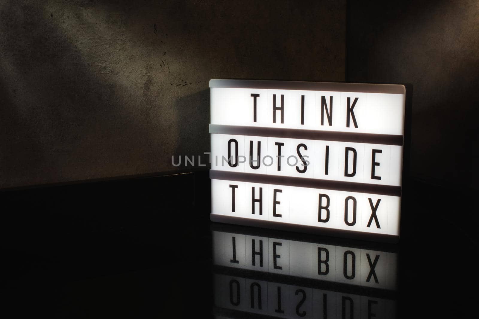 Think outside the box motivational message on a light box in a cinematic moody background