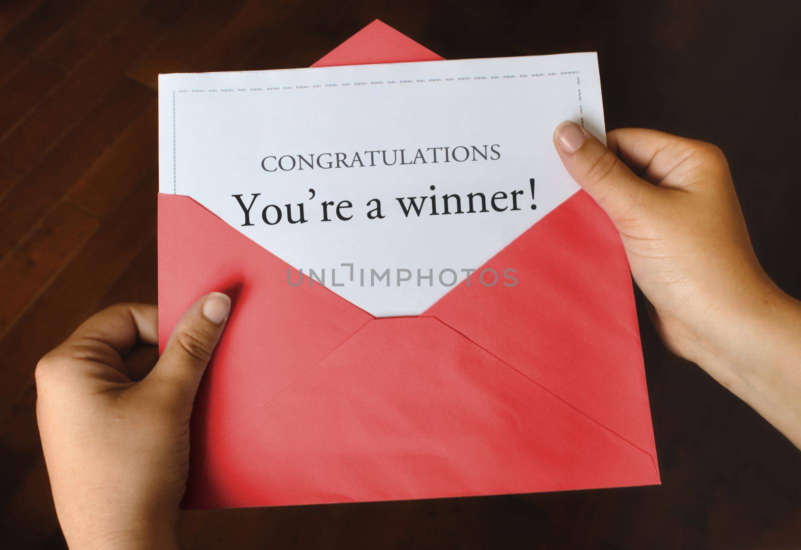 An open red envelope with a letter that says Congratulations You're a winner! with female hands holding it up