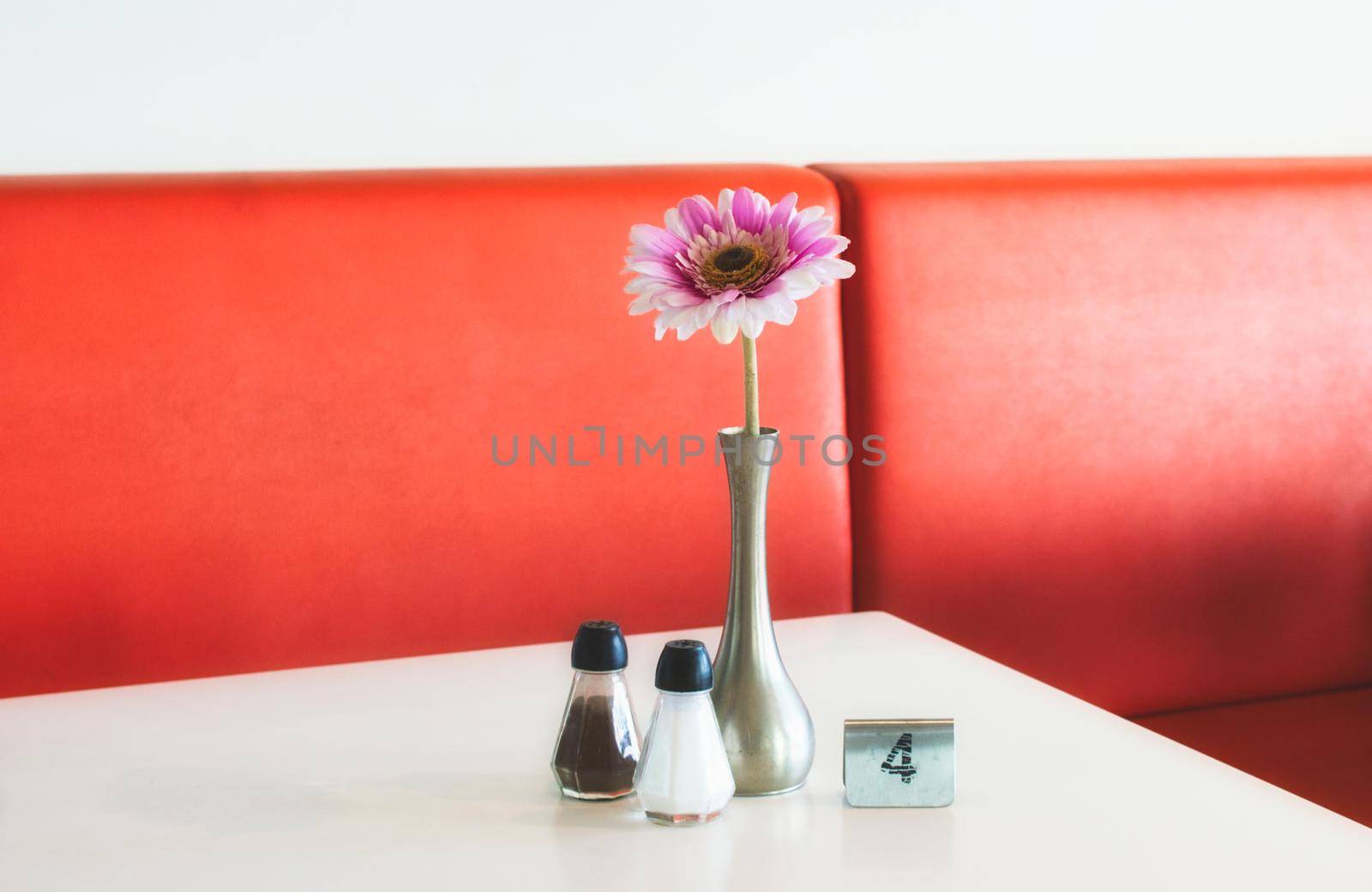 Indoor table setting in a cafe with flower in pot, salt and pepper shakers and metal number marker