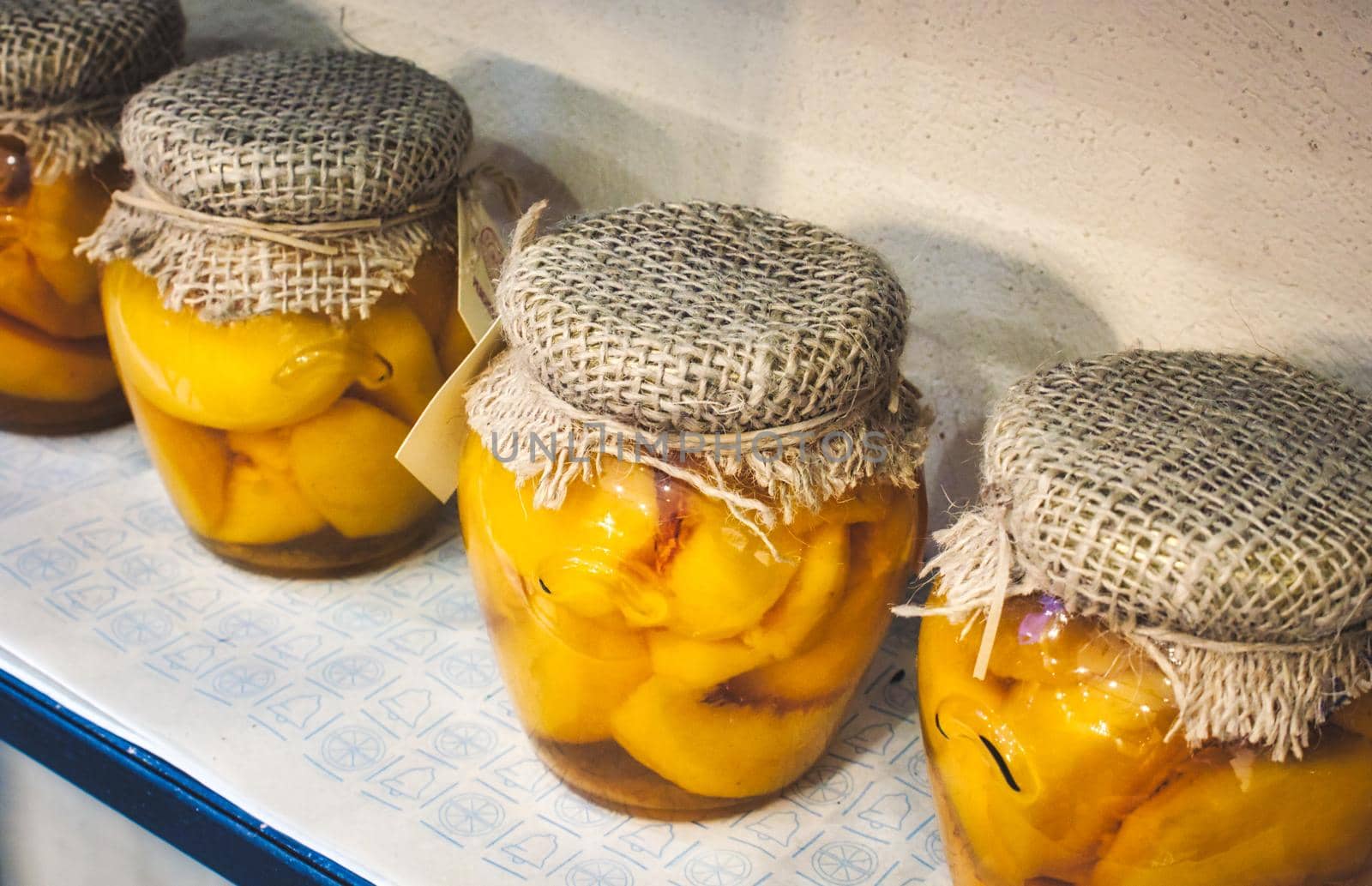 Glass jars of sliced peaches covered with sackcloth and tied with string in a row on a shelf