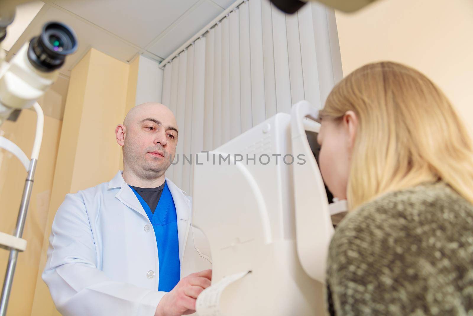 A male ophthalmologist checks the eyesight of a young girl using a modern vision tester by Yurich32